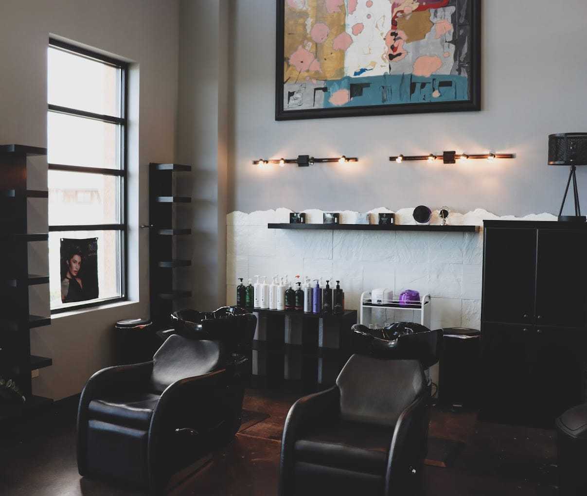 Modern hair salon interior with two black styling chairs and wall art.
